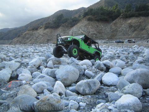 1987 Suzuki Samurai - A modified green off-road vehicle tackles a challenging rocky terrain, with other vehicles visible in the background.