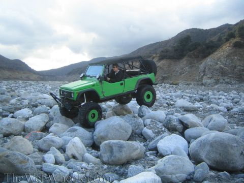 1987 Suzuki Samurai - A modified green off-road vehicle navigates a rocky terrain under a cloudy sky.