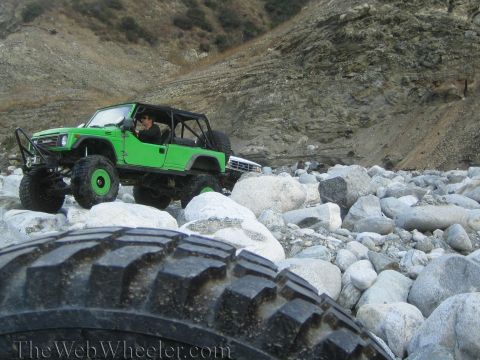 1987 Suzuki Samurai - A modified green off-road vehicle navigates a rocky terrain, with another vehicle partially visible in the background.