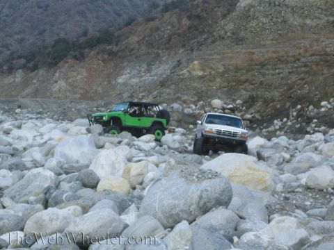 1987 Suzuki Samurai - Two modified off-road vehicles traverse a challenging rocky landscape, demonstrating their capabilities.