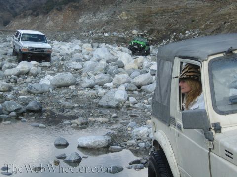 1987 Suzuki Samurai - Multiple off-road vehicles traverse a challenging rocky riverbed terrain.
