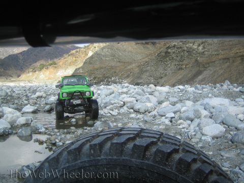 1987 Suzuki Samurai - 1987 Suzuki Samurai navigating a rocky riverbed with mountains in the background.