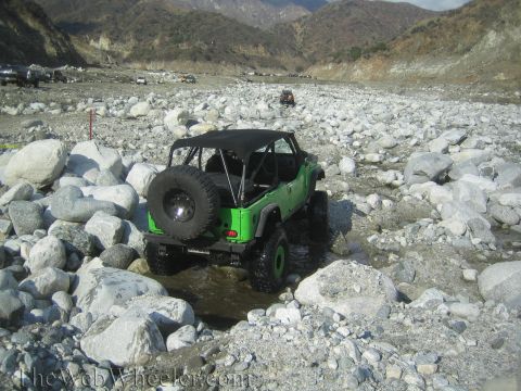 1987 Suzuki Samurai - A bright green Jeep navigates a rocky, dry riverbed with other vehicles in the distance.