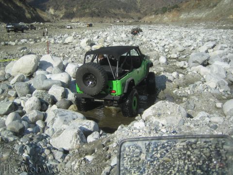 1987 Suzuki Samurai - Multiple off-road vehicles navigate a rocky, dry riverbed under a clear sky.