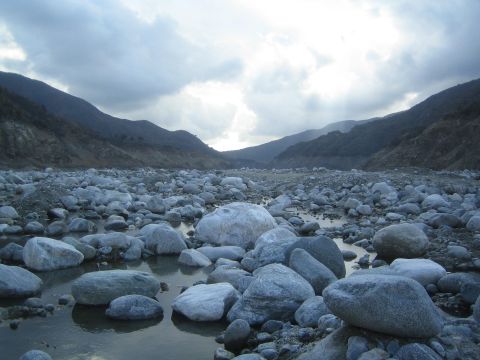 1987 Suzuki Samurai - A wide shot of a rocky riverbed with mountains in the background under a cloudy sky.