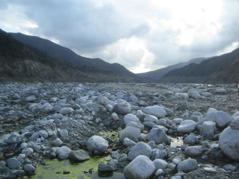 1987 Suzuki Samurai - A vast, rocky riverbed stretches towards distant mountains under a dramatic, cloudy sky.