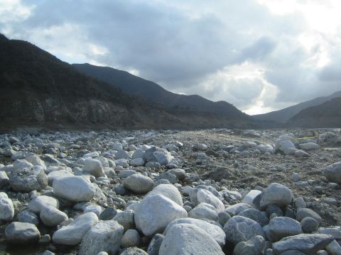 1987 Suzuki Samurai - A wide, rocky riverbed stretches towards distant mountains under a dramatic, cloudy sky.
