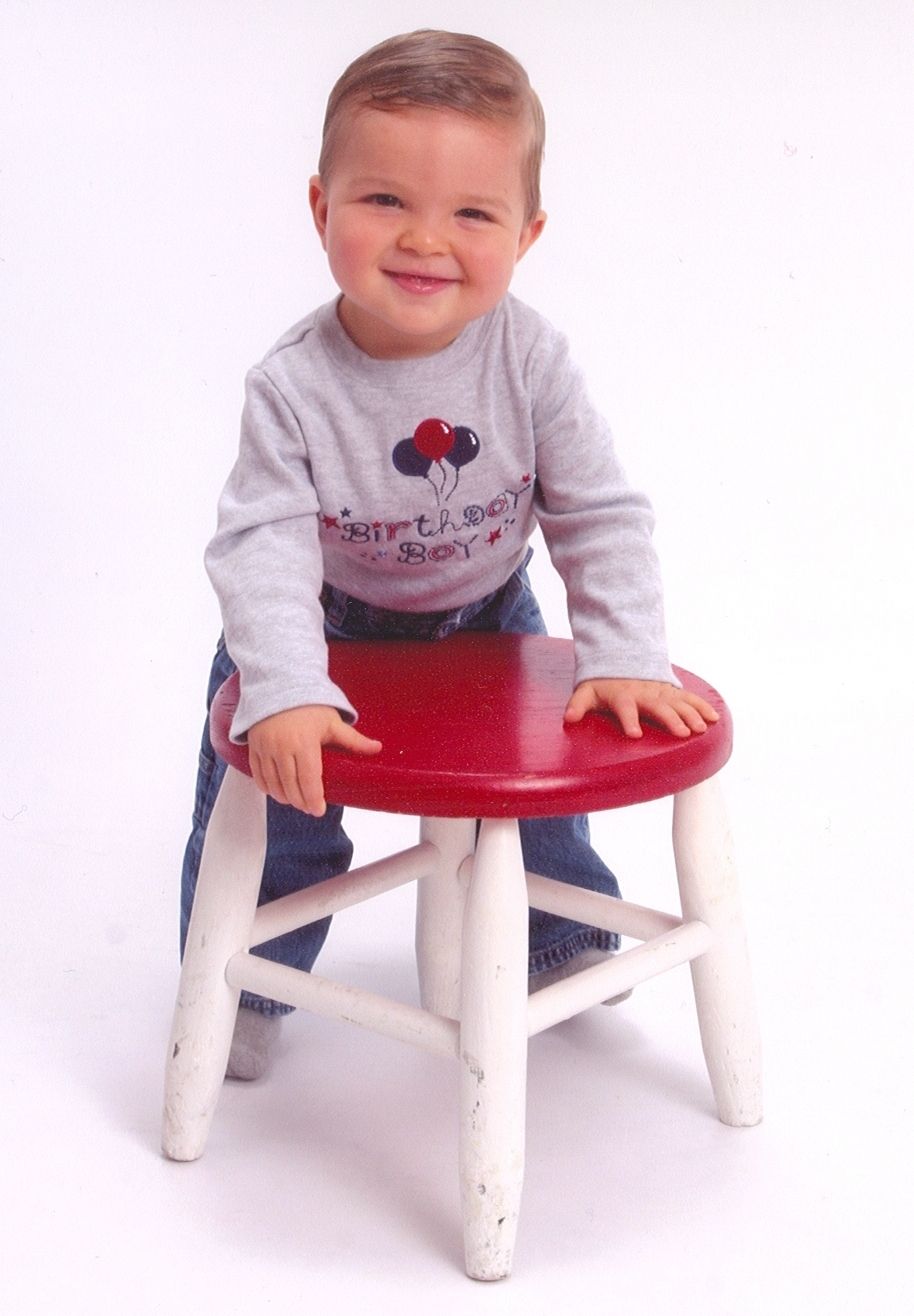 Toddler in Birthday Boy shirt standing behind a red and white stool