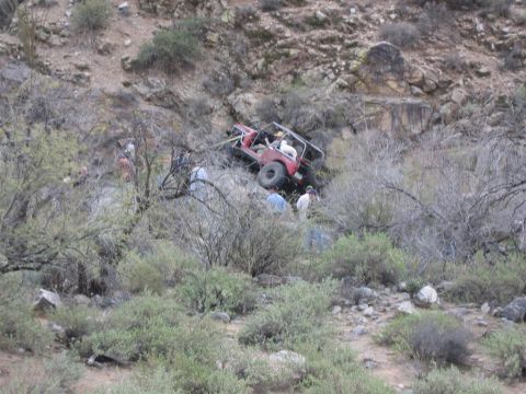 1987 Suzuki Samurai - A red 1987 Suzuki Samurai is stuck on a rocky incline, surrounded by several individuals observing the situation.