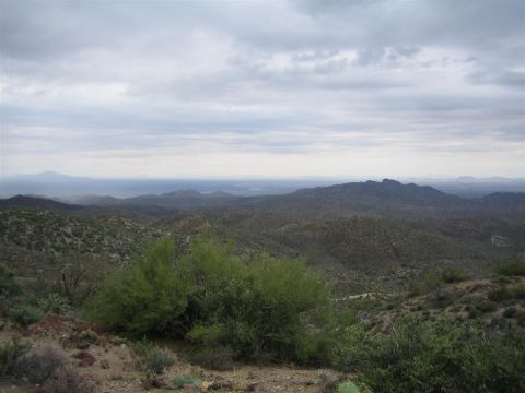 1987 Suzuki Samurai - A wide view of a desert landscape under a cloudy sky, with scrub brush and cacti in the foreground.