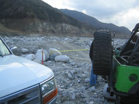 1987 Suzuki Samurai - Two off-road vehicles parked in a rocky terrain with mountains in the background.