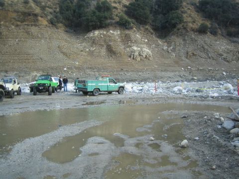1987 Suzuki Samurai - Multiple vehicles are gathered in a muddy, outdoor scene with a steep, rocky hillside behind them.
