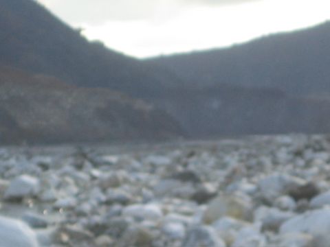 1987 Suzuki Samurai - A rocky riverbed stretches towards distant mountains under a cloudy sky.