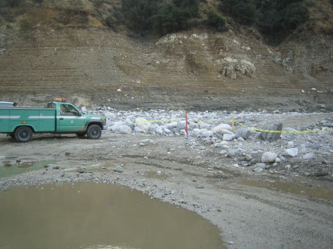 1987 Suzuki Samurai - A green utility truck is parked on a dirt road with a muddy puddle in the foreground and a rocky hillside in the background.