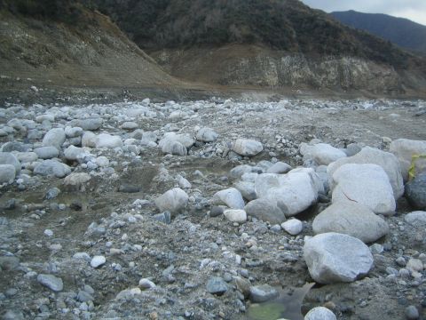 1987 Suzuki Samurai - A wide shot of a barren landscape filled with rocks and debris, suggesting a dry riverbed or landslide area.