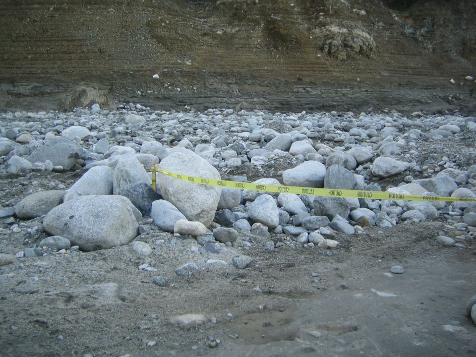Yellow caution tape stretches across a rocky, uneven ground with a dirt embankment in the background