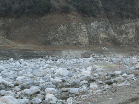 1987 Suzuki Samurai - A wide view of a dry riverbed filled with stones, leading up to a barren, rocky hillside.