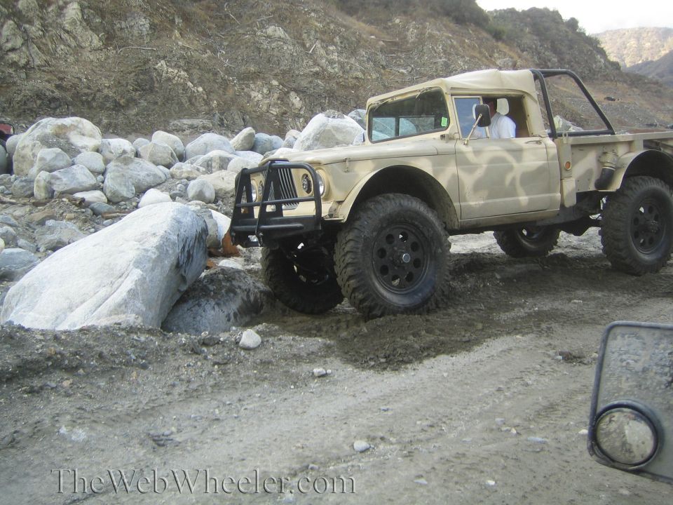 Jeep M715 truck with camouflage paint, driving over rocks and dirt
