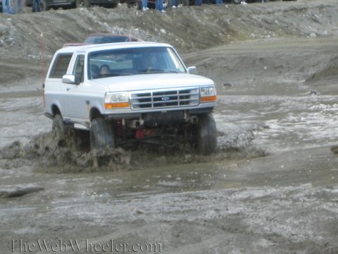 1987 Suzuki Samurai - A Ford Bronco navigates a muddy obstacle course, splashing water as it goes.