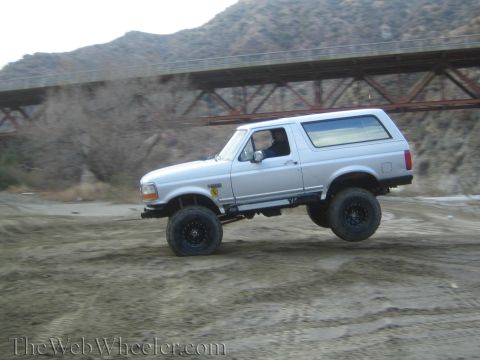 1987 Suzuki Samurai - This lifted Ford Bronco is kicking up dust while driving on a dirt path near a bridge.