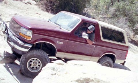 1993 Ford Bronco - This maroon Ford Bronco with tan trim is shown off-road, demonstrating its capability on rough terrain.