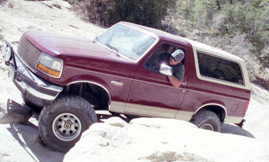 Maroon Ford Bronco with tan trim navigating rocky terrain, front-left angle