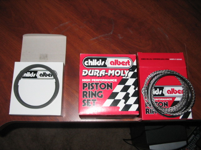 Three boxes of Childs & Albert piston rings on a wooden surface. One box is open with rings inside