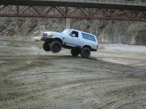 1987 Suzuki Samurai - A white 1992 Ford Bronco is captured mid-air while off-roading under a bridge.
