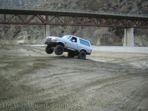 1987 Suzuki Samurai - Ford Bronco is shown off-roading on a dirt path with a bridge overhead.
