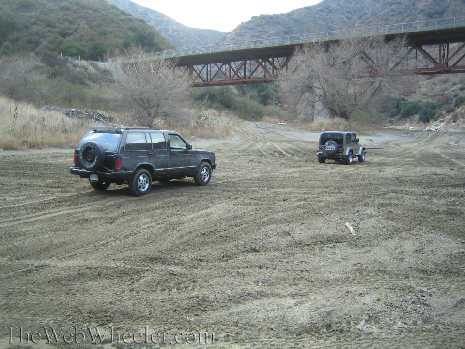 Dark SUV and Jeep in a dry riverbed under a bridge