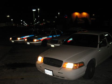 2003 Ford Crown Victoria - Multiple police vehicles are parked in a lot under streetlights at night.