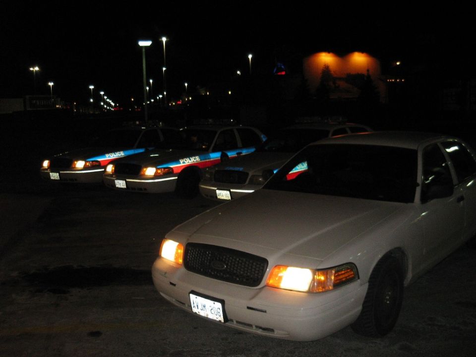 Several police cars parked in a lot at night. One white car is in the foreground