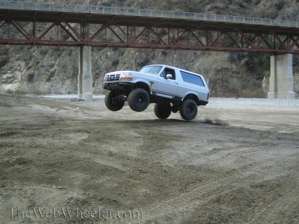 White Ford Bronco mid-air jump, lifted suspension, off-road tires, under a bridge