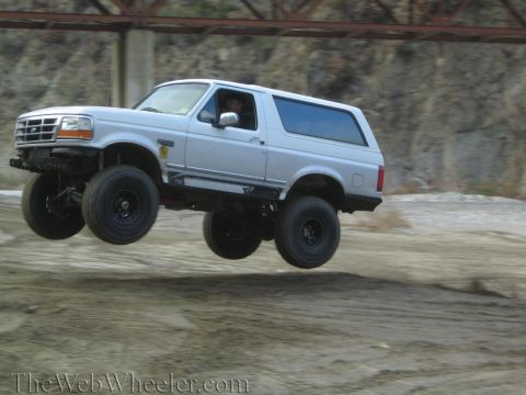 1987 Suzuki Samurai - This lifted Ford Bronco is captured mid-air during an off-road jump, its modified suspension and large tires.