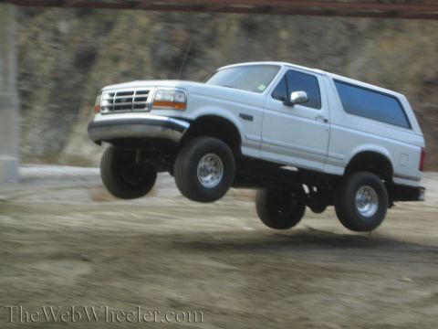 1987 Suzuki Samurai - White Ford Bronco airborne during a jump, showing its front grille and side profile.