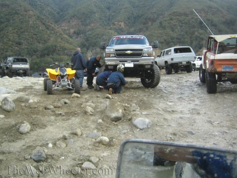1987 Suzuki Samurai - A group of off-road vehicles are parked on a rocky trail, with some people attending to a large pickup truck.