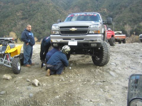 1987 Suzuki Samurai - Several people are gathered around the front of a lifted silver Chevrolet Silverado pickup truck in a rocky, outdoor setting.