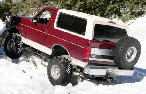 1993 Ford Bronco - This red and white Ford Bronco is equipped with off-road tires and is navigating a snowy incline.