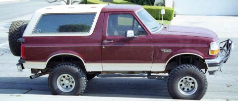 1993 Ford Bronco - This two-tone Ford Bronco is parked on a street with a manicured hedge in the background.