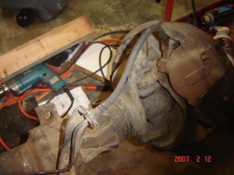 1993 Ford Bronco - A rear axle assembly with brake caliper and brake lines is shown, along with a drill and wood.