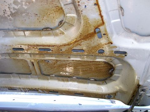 1992 Ford Bronco - Close-up of a silver underbody or inner-fender panel coated in a heavy brown oil film, with the fluid pooling in the stamped channels and r…