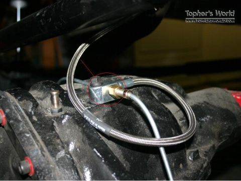 1992 Ford Bronco - A braided brake line is connected to a fitting on the rear axle assembly of a vehicle.