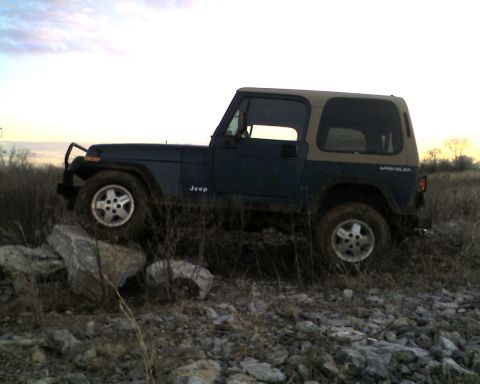 1995 Ford Bronco - A Jeep Wrangler navigates a rocky, off-road path under a cloudy sky.