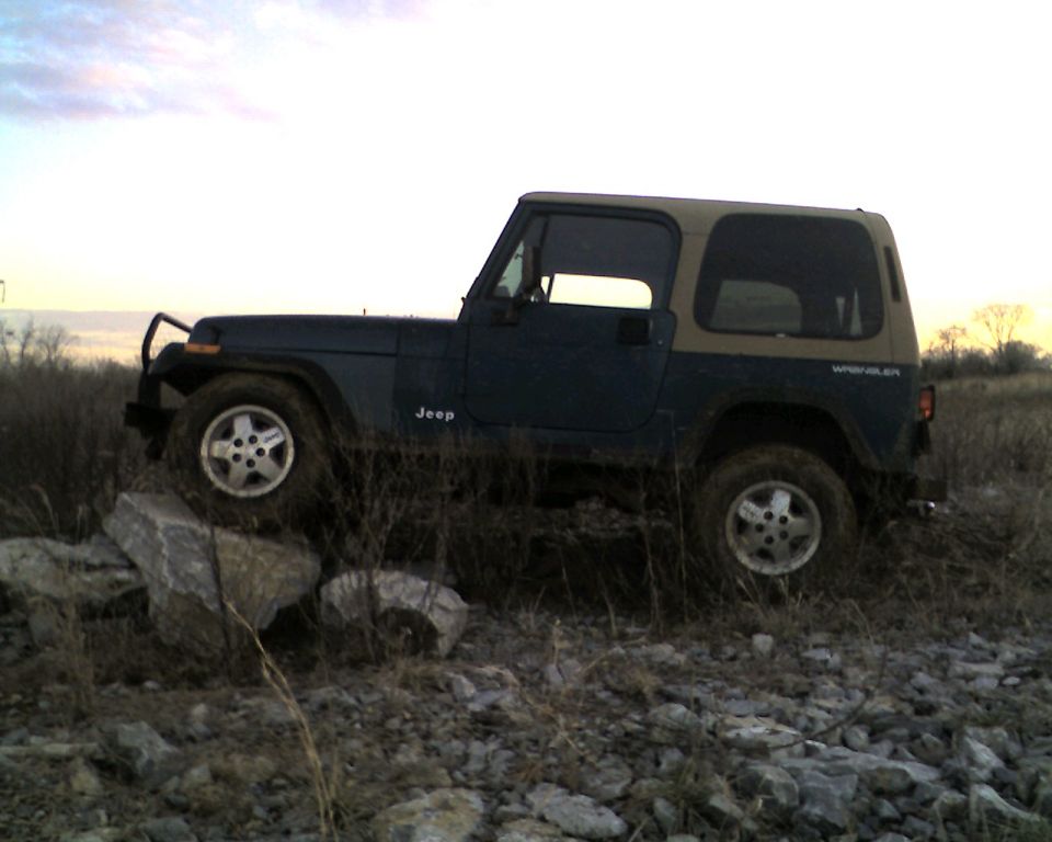 Dark green Jeep Wrangler with tan top on rocky terrain