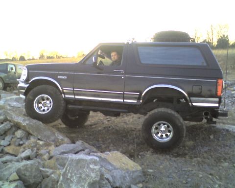 1995 Ford Bronco - Black lifted Ford Bronco crawling over rocky ground with a driver seated inside looking out the open window, shot from the driver's side in…
