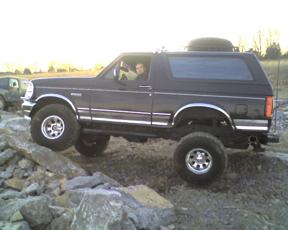 Black lifted Ford Bronco with driver crawling over rocks, side view