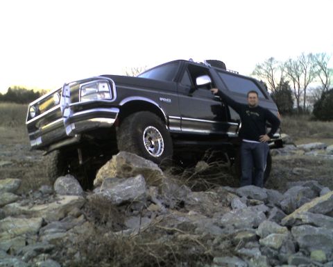 1995 Ford Bronco - Black lifted Ford Bronco tipped up on a rock pile with a person in a dark shirt and jeans standing alongside the rear quarter for scale. Th…