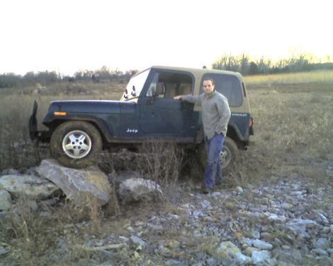 1995 Ford Bronco - Man poses with a Jeep Wrangler that is partially on rocks in an outdoor setting.