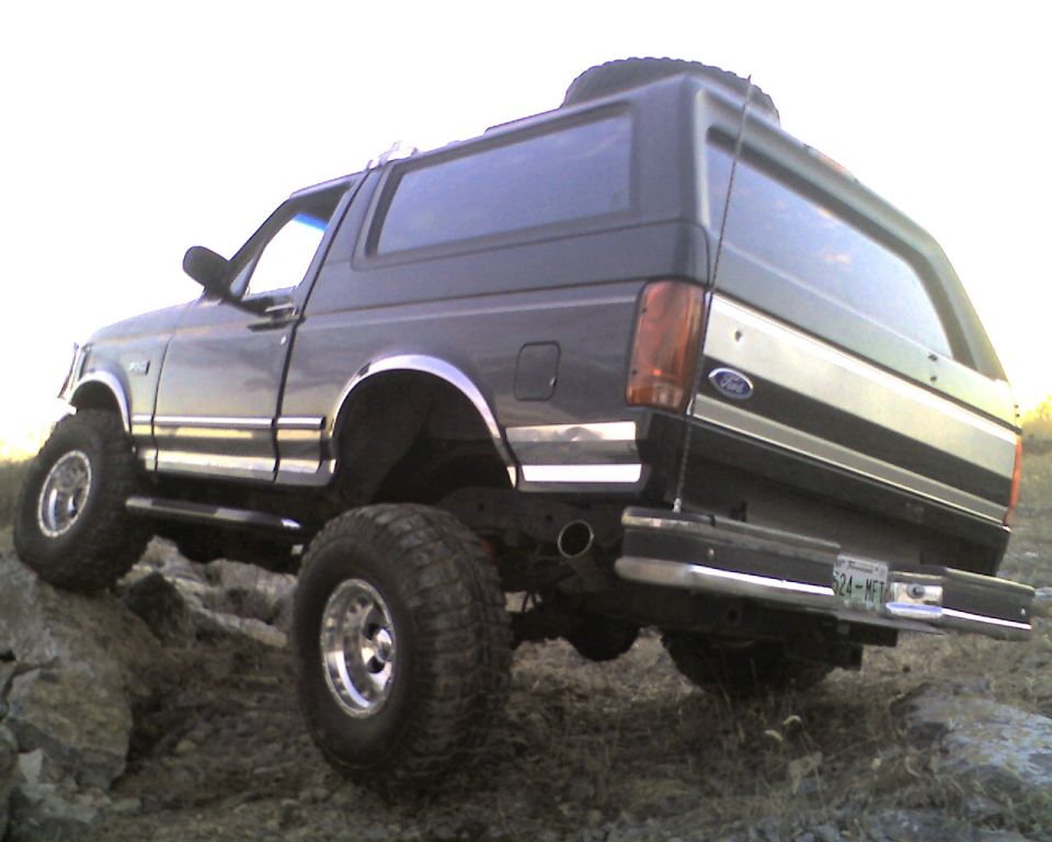 Black lifted Ford Bronco flexing over rocks, rear three-quarter low angle
