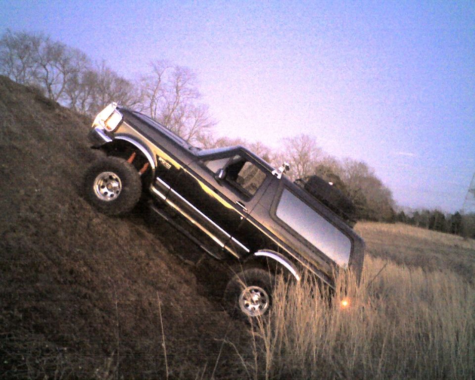 Lifted black Ford Bronco climbing a steep dirt hill, passenger-side view
